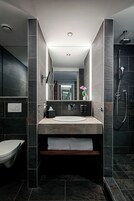 Uma casa de banho moderna com um espelho grande, uma pia, uma sanita e um chuveiro.