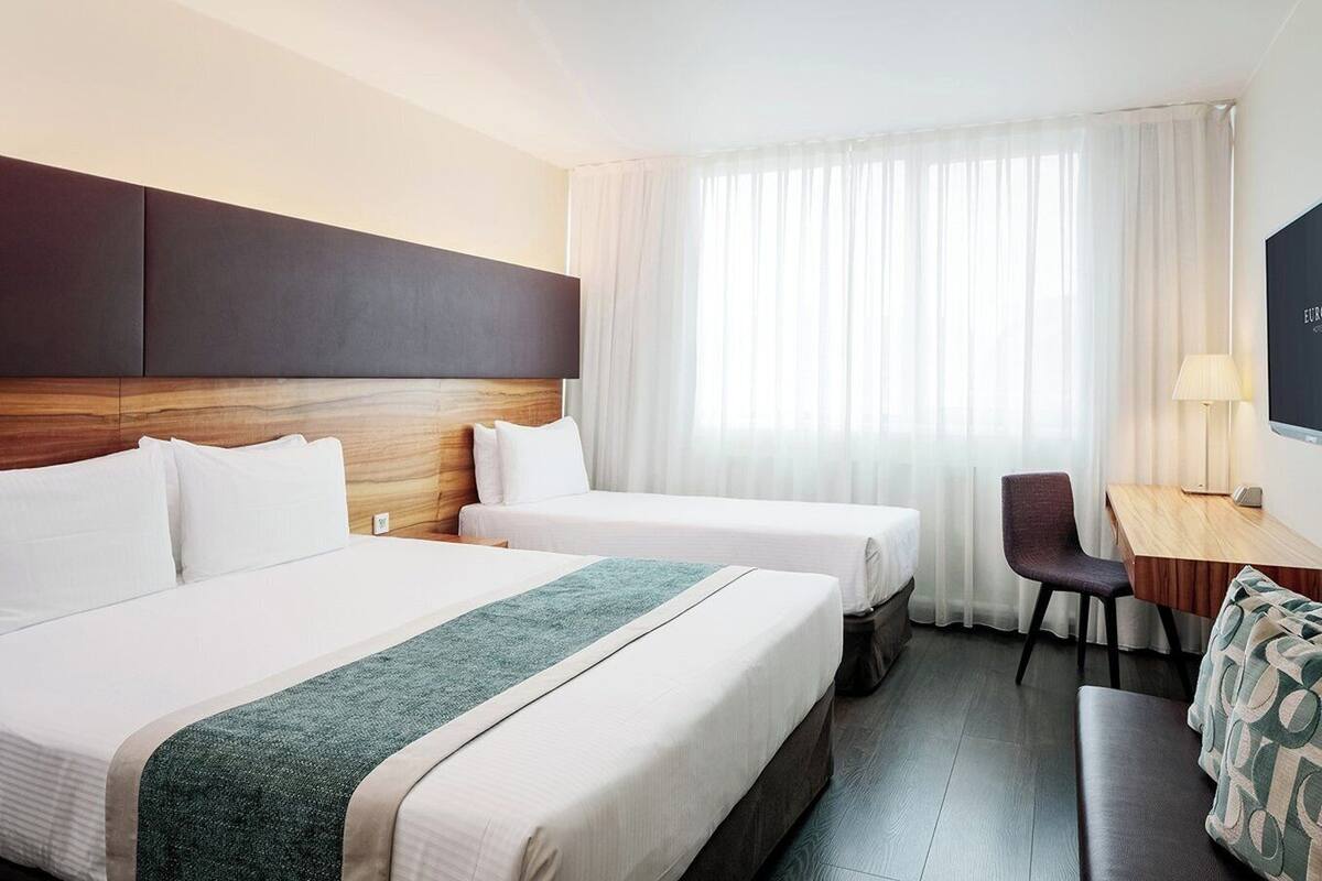 Habitación de hotel con dos camas individuales, un escritorio, una silla y un televisor.