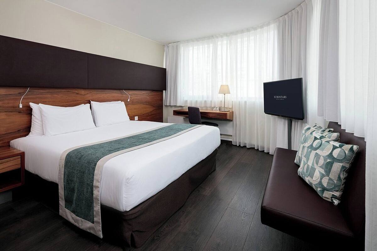 Una habitación de hotel con una cama grande, un escritorio, una silla, un televisor y un sofá.