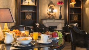 A breakfast table with croissants, fruit, and juice, set in a room with a fireplace and bookshelves. - Hôtel Villa Glamour (Paris)