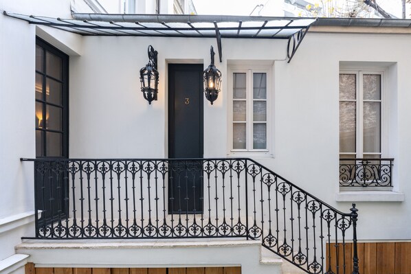 Un bâtiment blanc avec une porte noire, deux lanternes noires et un garde-corps de balcon en fer forgé noir.