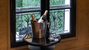 A metal bucket with a bottle of champagne and two glasses on a table by a window with a black iron railing. - Hôtel Villa Glamour (Paris)