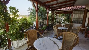 An outdoor patio with wicker furniture and a tiled floor, surrounded by greenery. - Angela Apartments (Samos)