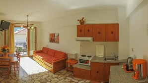 A compact living space with a sofa, dining table, kitchenette, and a balcony with a view. - Angela Apartments (Samos)