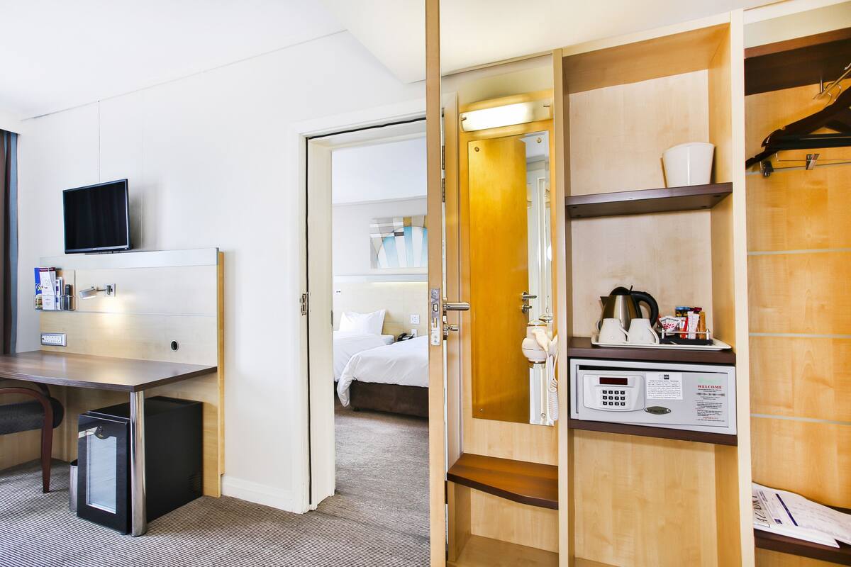 A hotel room with a desk, a television, a minibar, a bed, and a bathroom with a shower and a toilet.