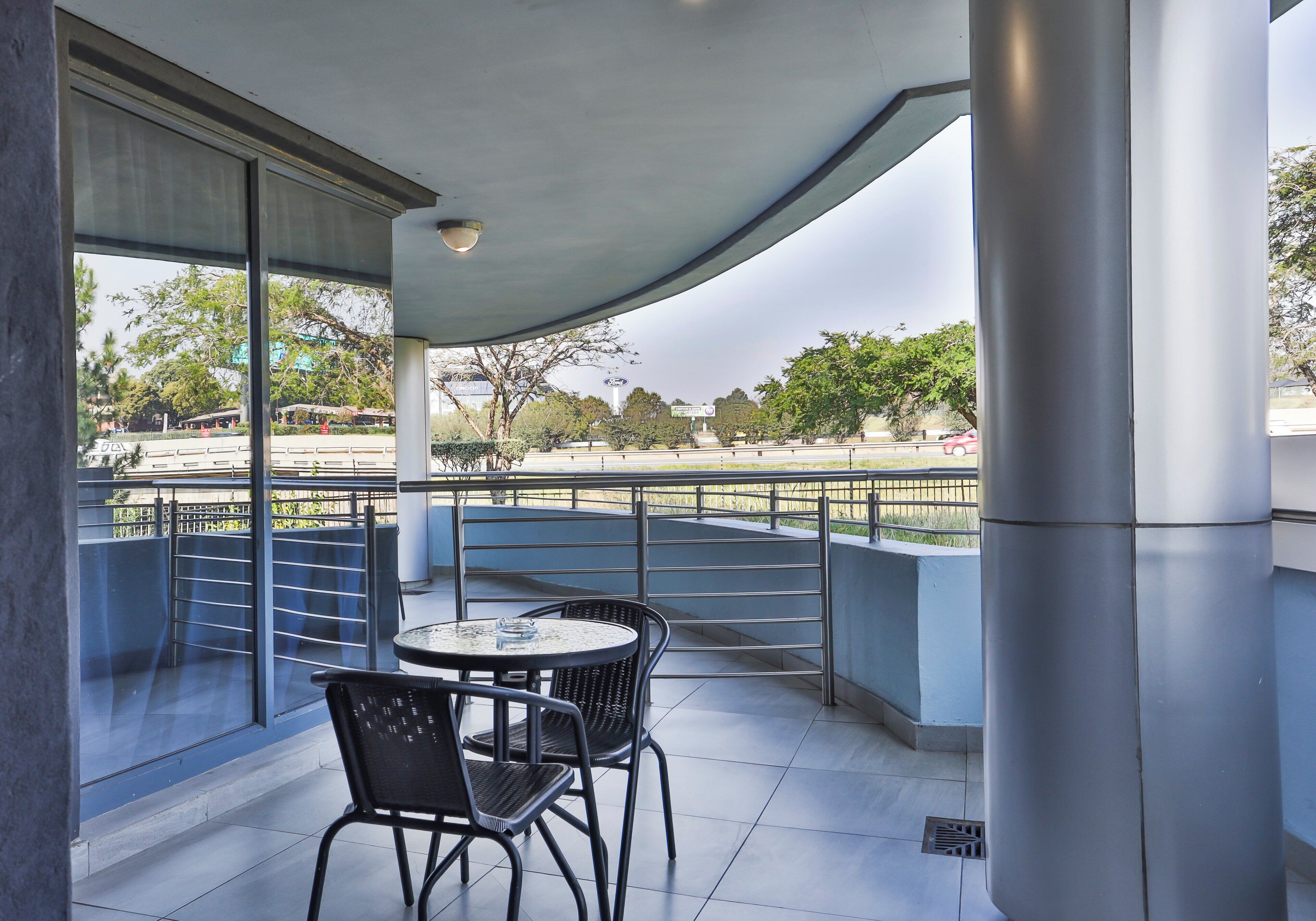 A covered outdoor seating area with a table and chairs, overlooking a parking lot and trees.