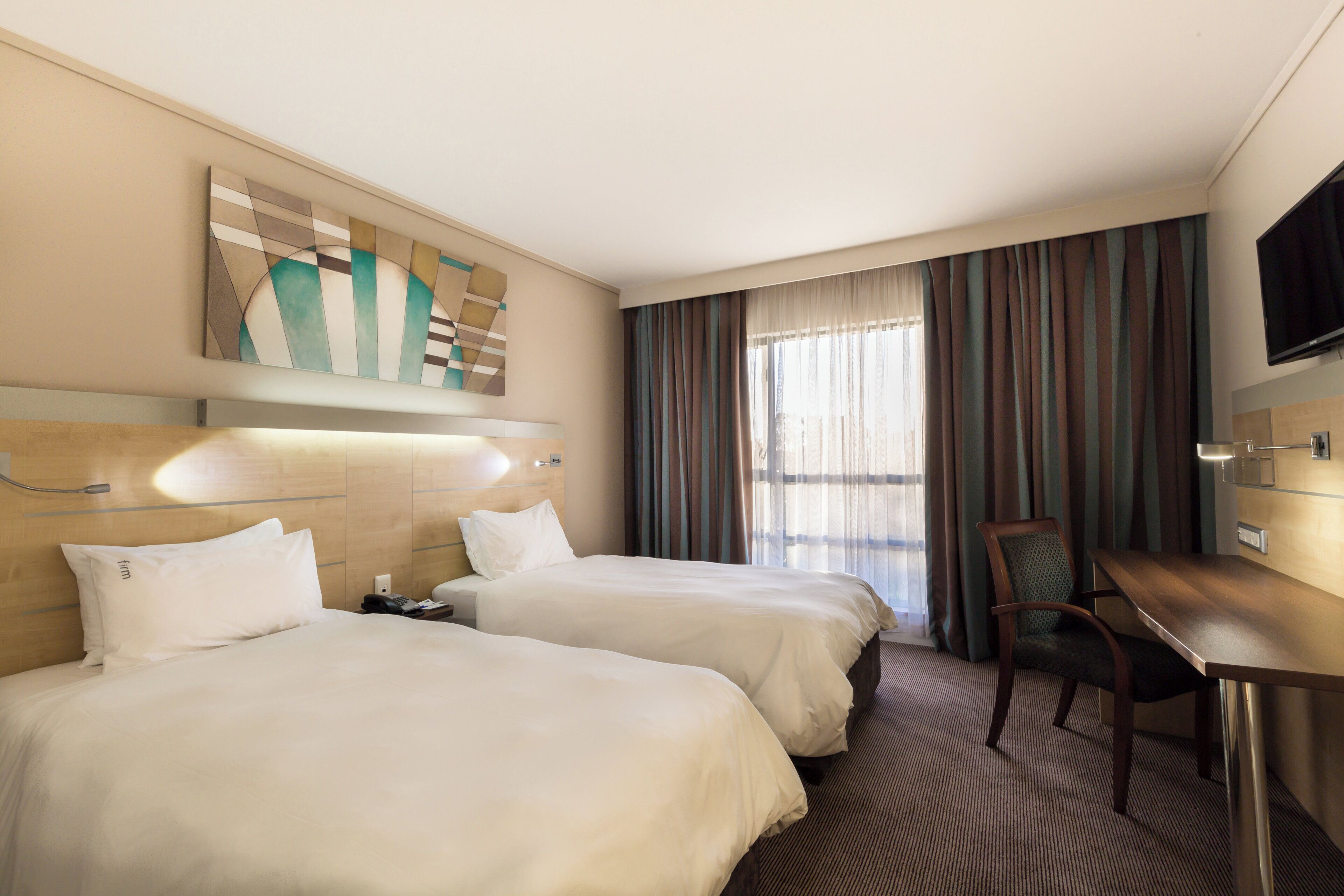Une chambre d’hôtel avec deux lits, un bureau, une chaise, une télévision et une grande fenêtre avec des rideaux.