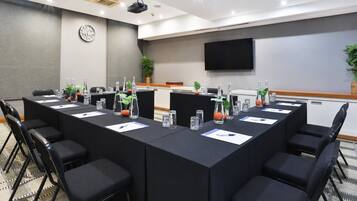 Un salón de conferencias con una mesa larga, sillas, botellas de agua y un reloj en la pared.