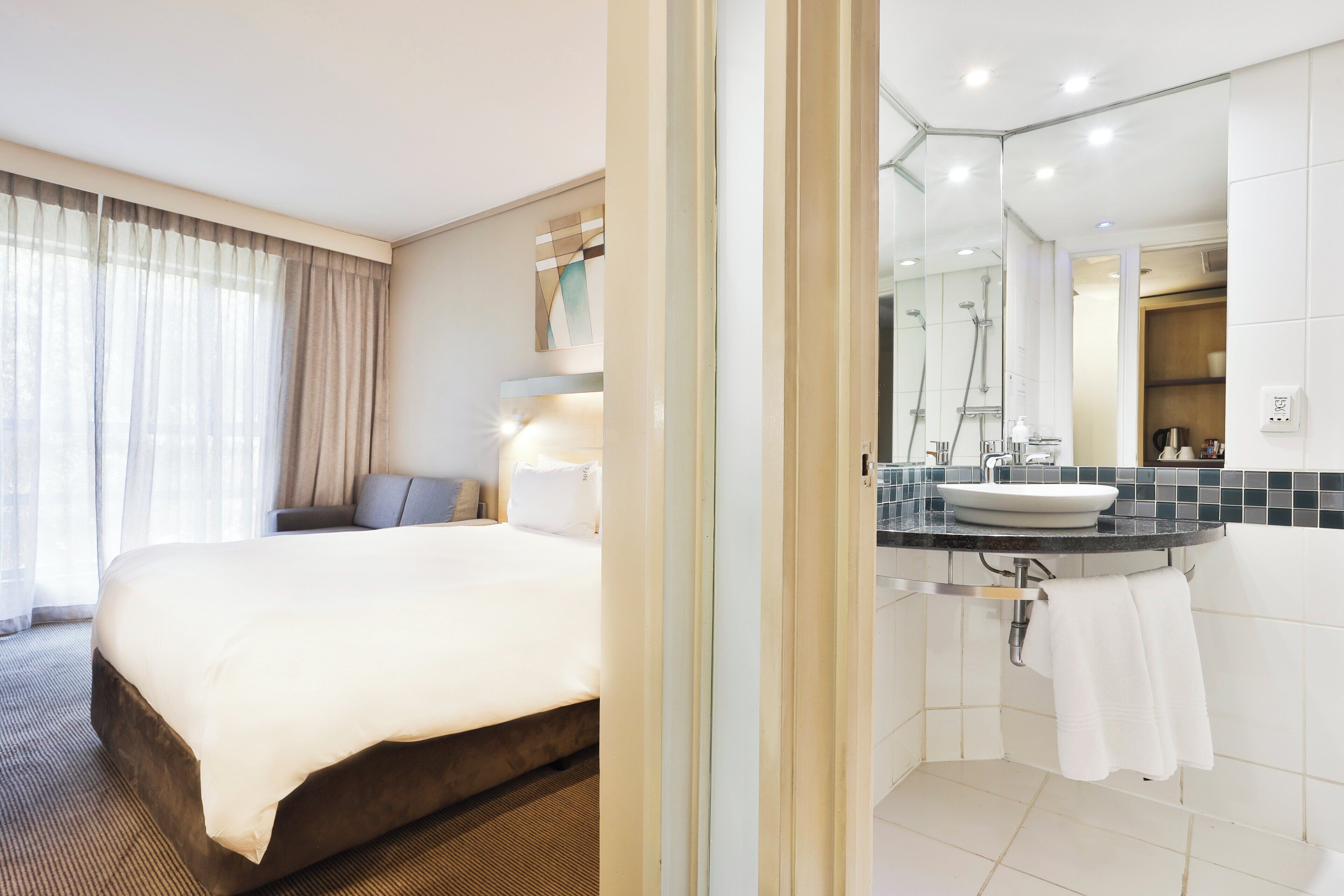 Ein Hotelzimmer mit einem Bett, einem Badezimmer mit Waschbecken und Spiegel sowie einer Dusche.