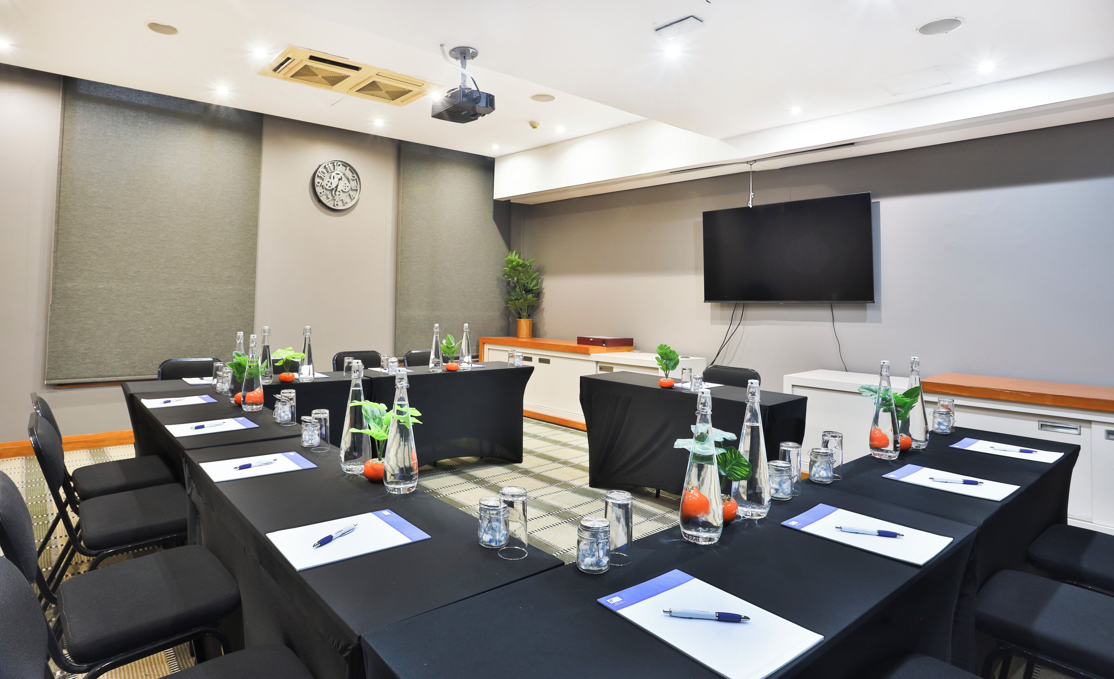 A conference room with a long table, chairs, a clock, a TV, and a plant.
