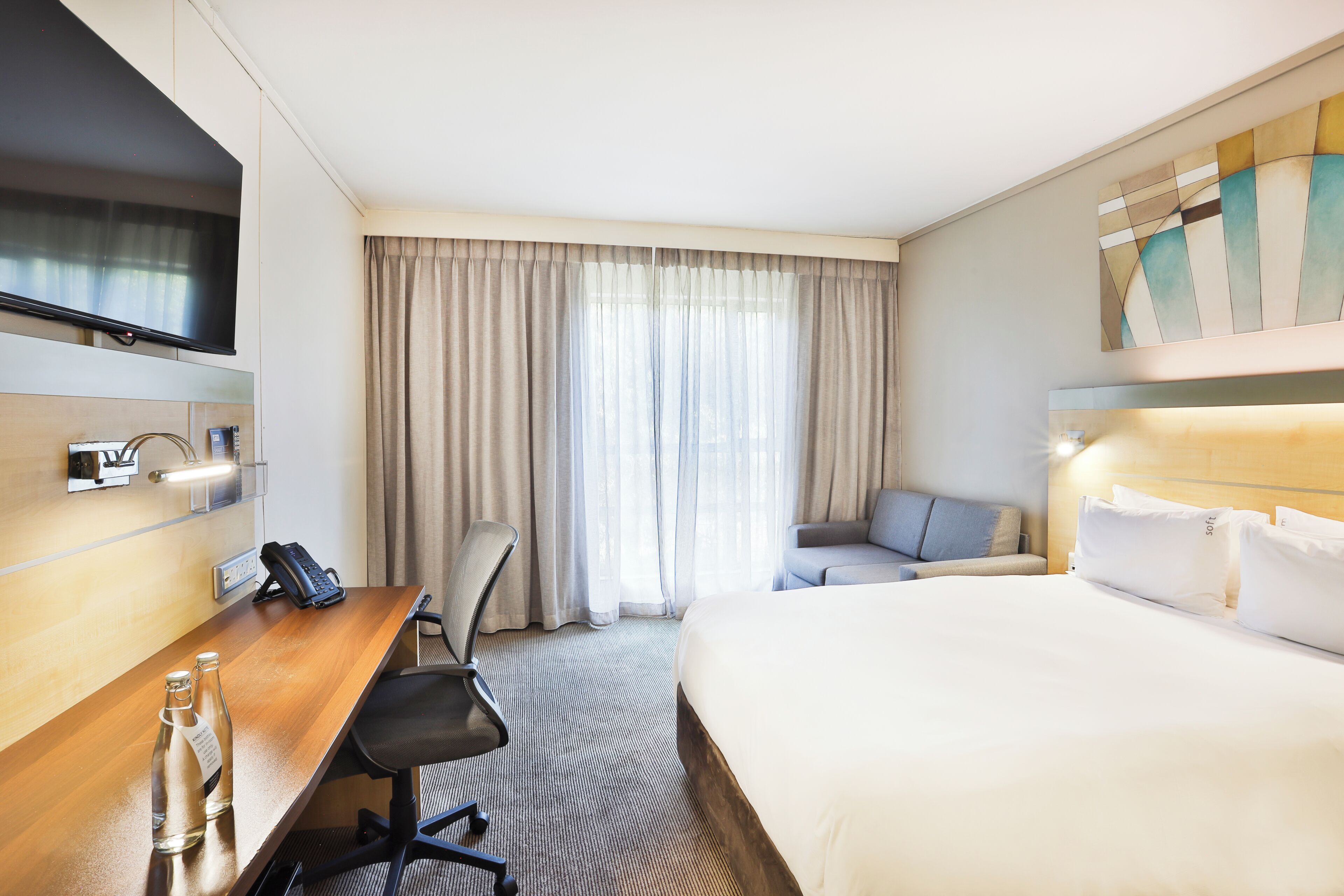 Habitación de hotel con cama, escritorio con teléfono, una silla y televisión montada en la pared.