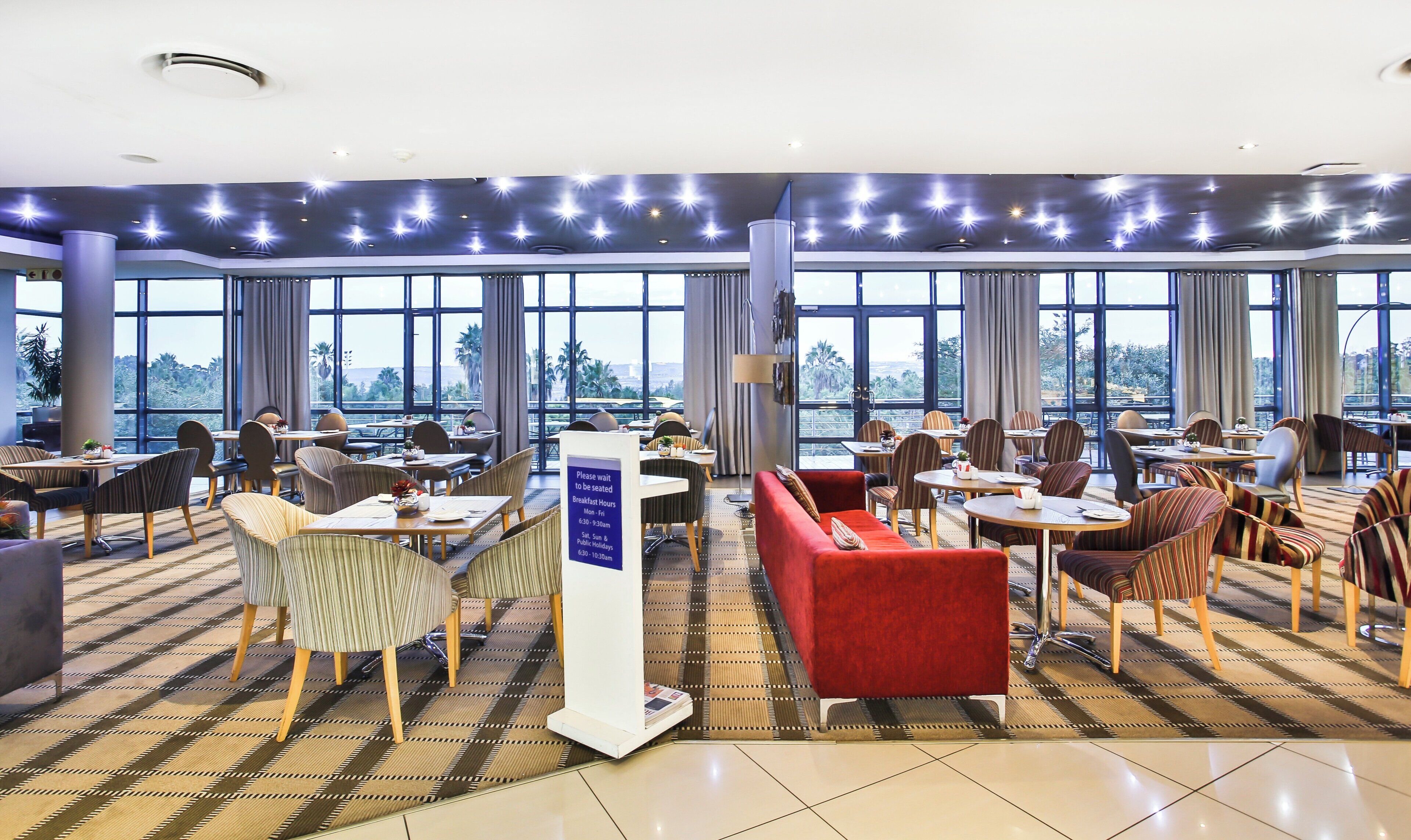A hotel dining area with tables, chairs, and a sign indicating breakfast hours.