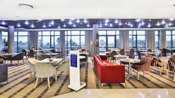 A hotel dining area with tables, chairs, and a sign indicating breakfast hours.