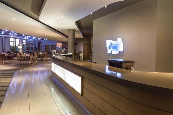 A modern hotel lobby with a reception desk, seating area, and a large digital display. - Holiday Inn Express Sandton Woodmead by IHG (Sandton)