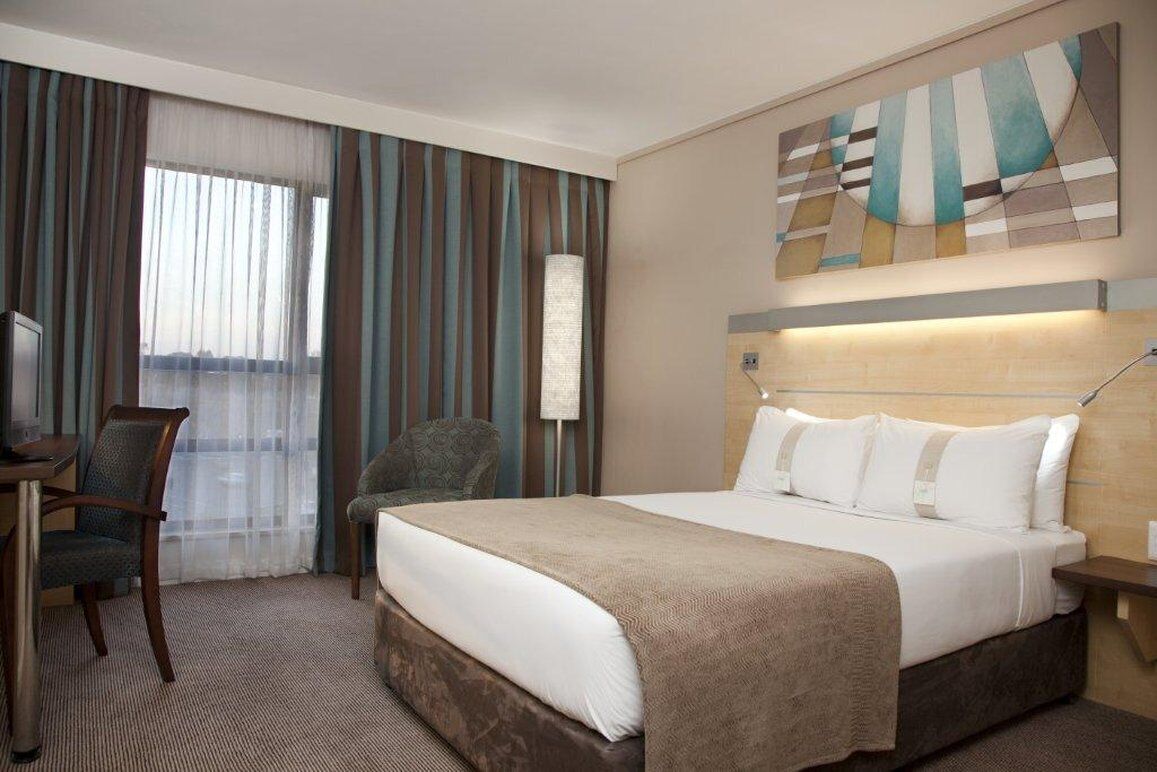 Une chambre d’hôtel avec un grand lit, un bureau avec une chaise, une lampe et une vue par la fenêtre.