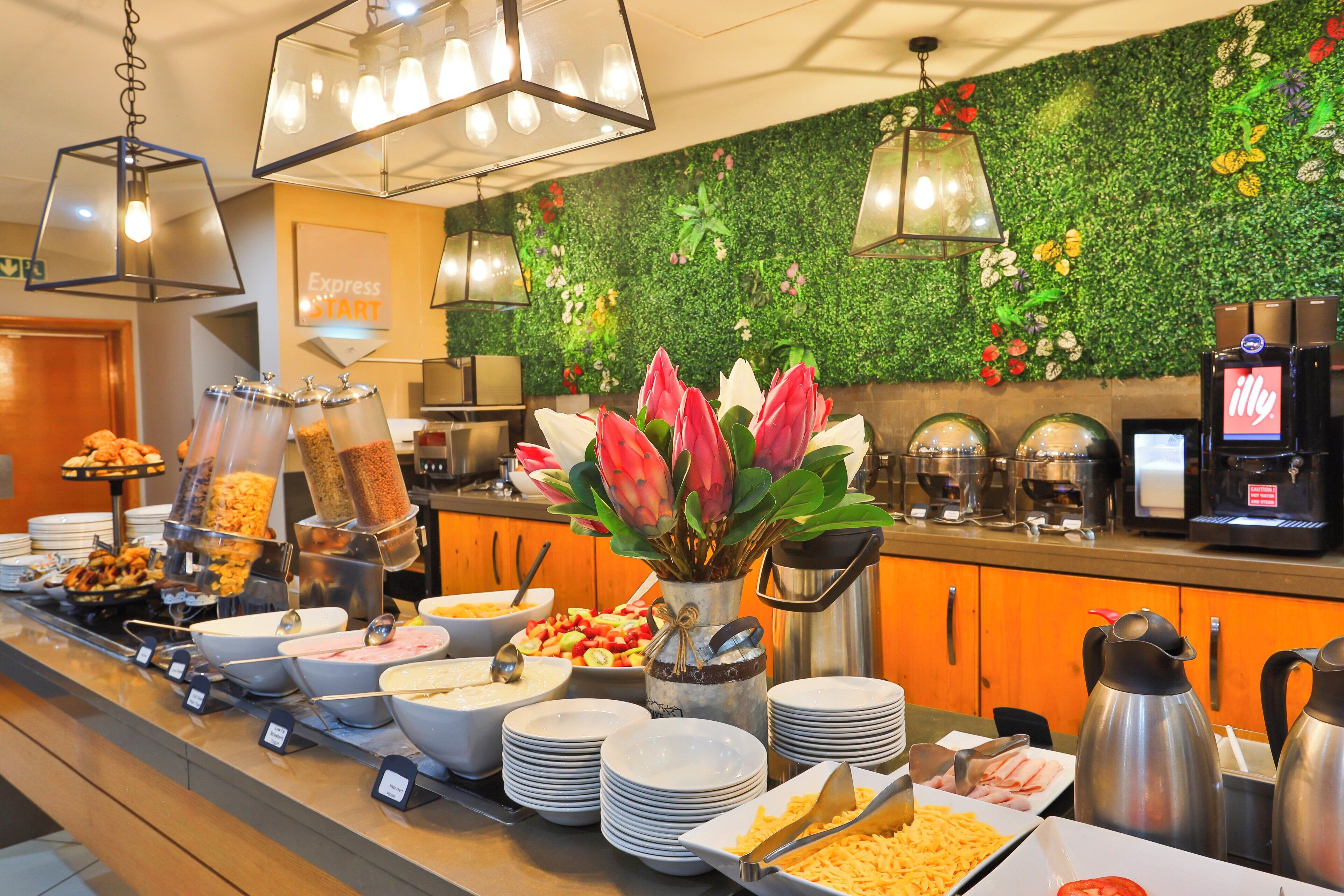 A buffet setup with various food options and a green wall with plants.
