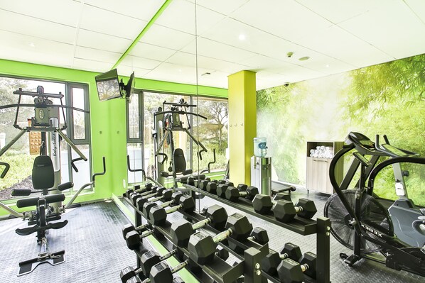 Et fitnesscenter med forskellig træningsudstyr, heriblandt håndvægte, et løbebånd og styrkemaskiner.