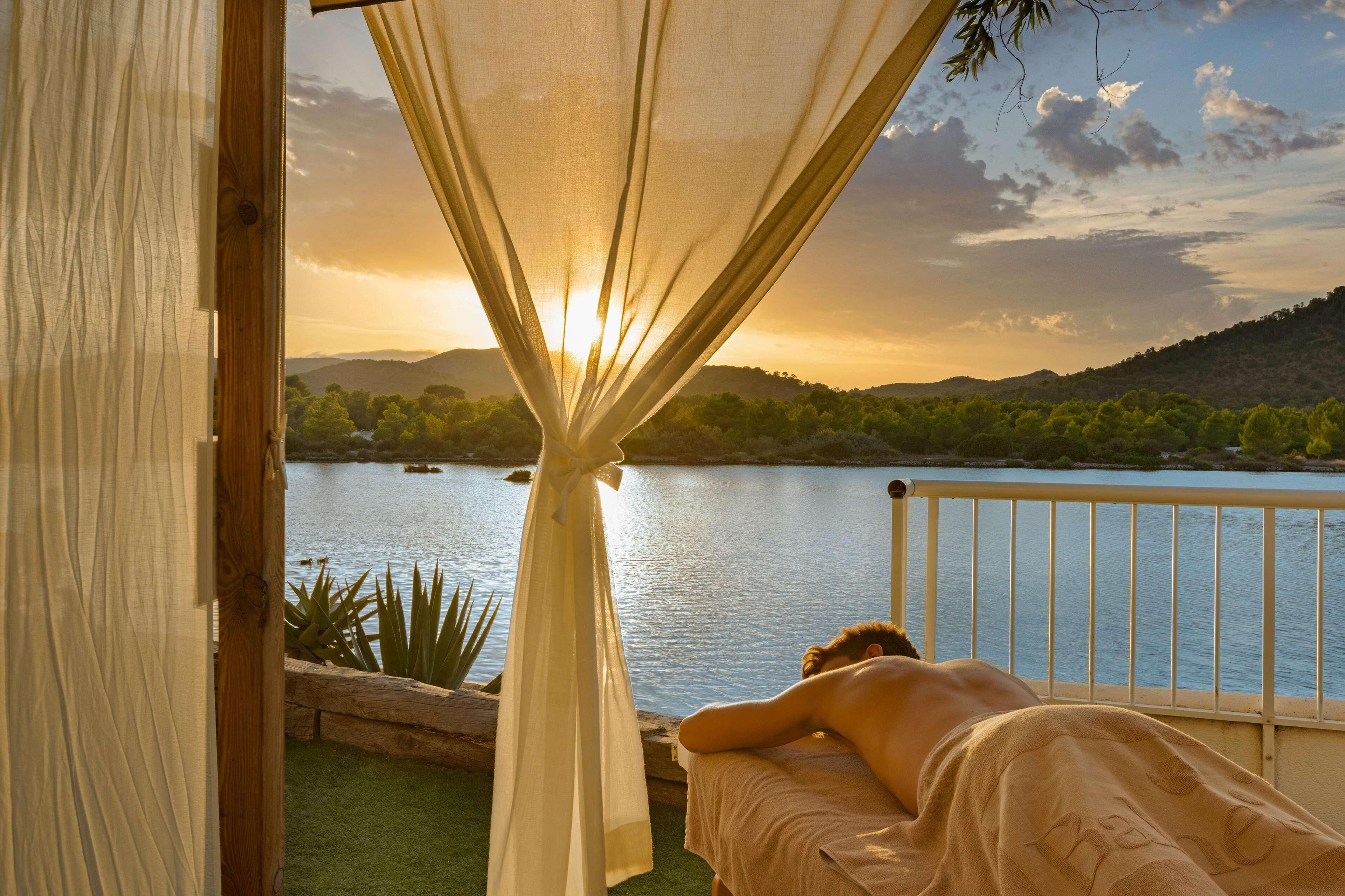 Eine Person entspannt im Bett mit Blick auf einen See und Berge.