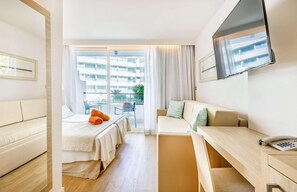 Une chambre d’hôtel équipée d’un lit, d’un bureau, d’une chaise, d’une télévision et d’une fenêtre donnant sur un immeuble.