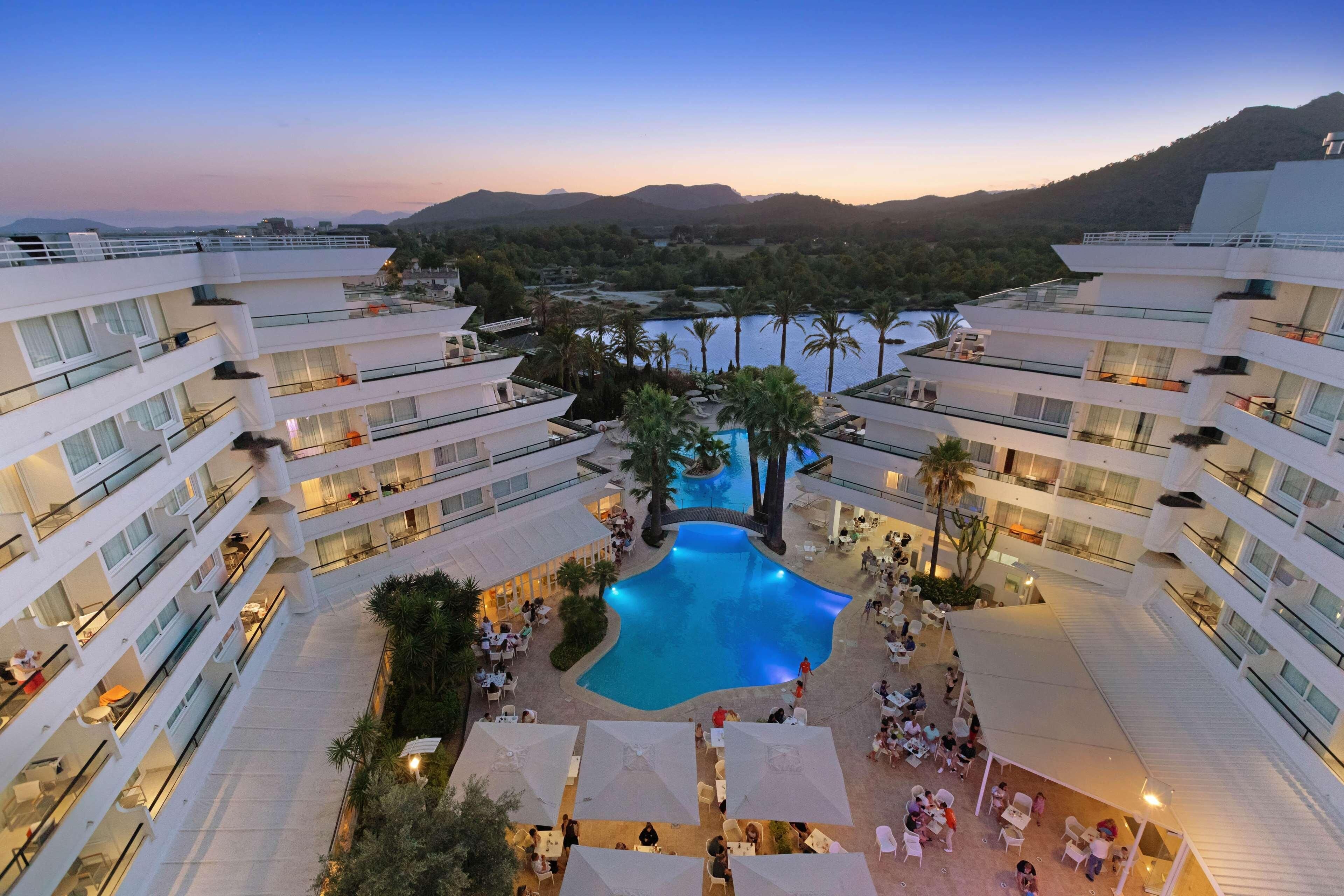 Un hotel amb piscina central envoltat de zones d'estar exteriors i nombrosos balcons.