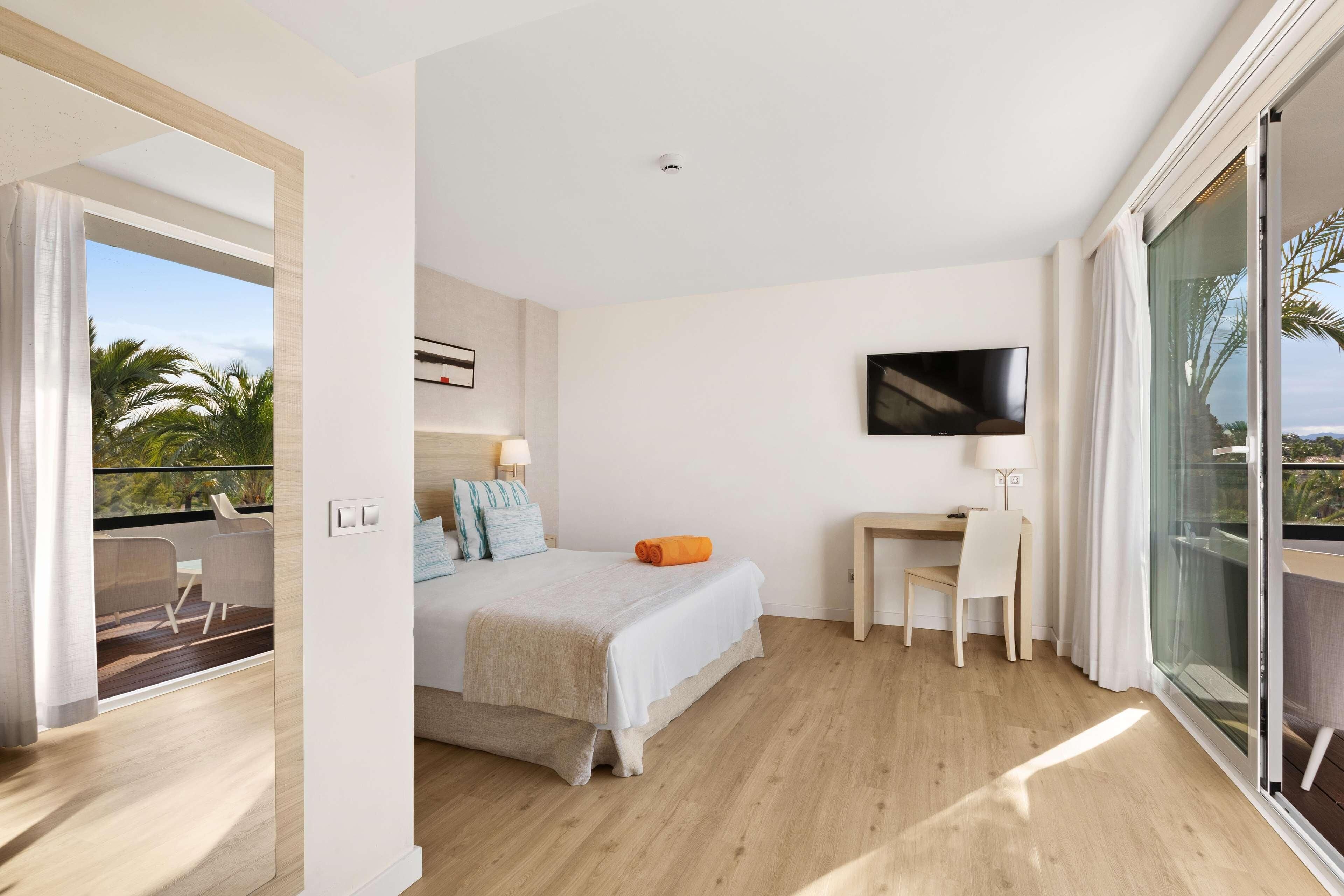 Ein modernes Hotelzimmer mit Balkon, einem Bett, einem Schreibtisch und einem Fernseher.