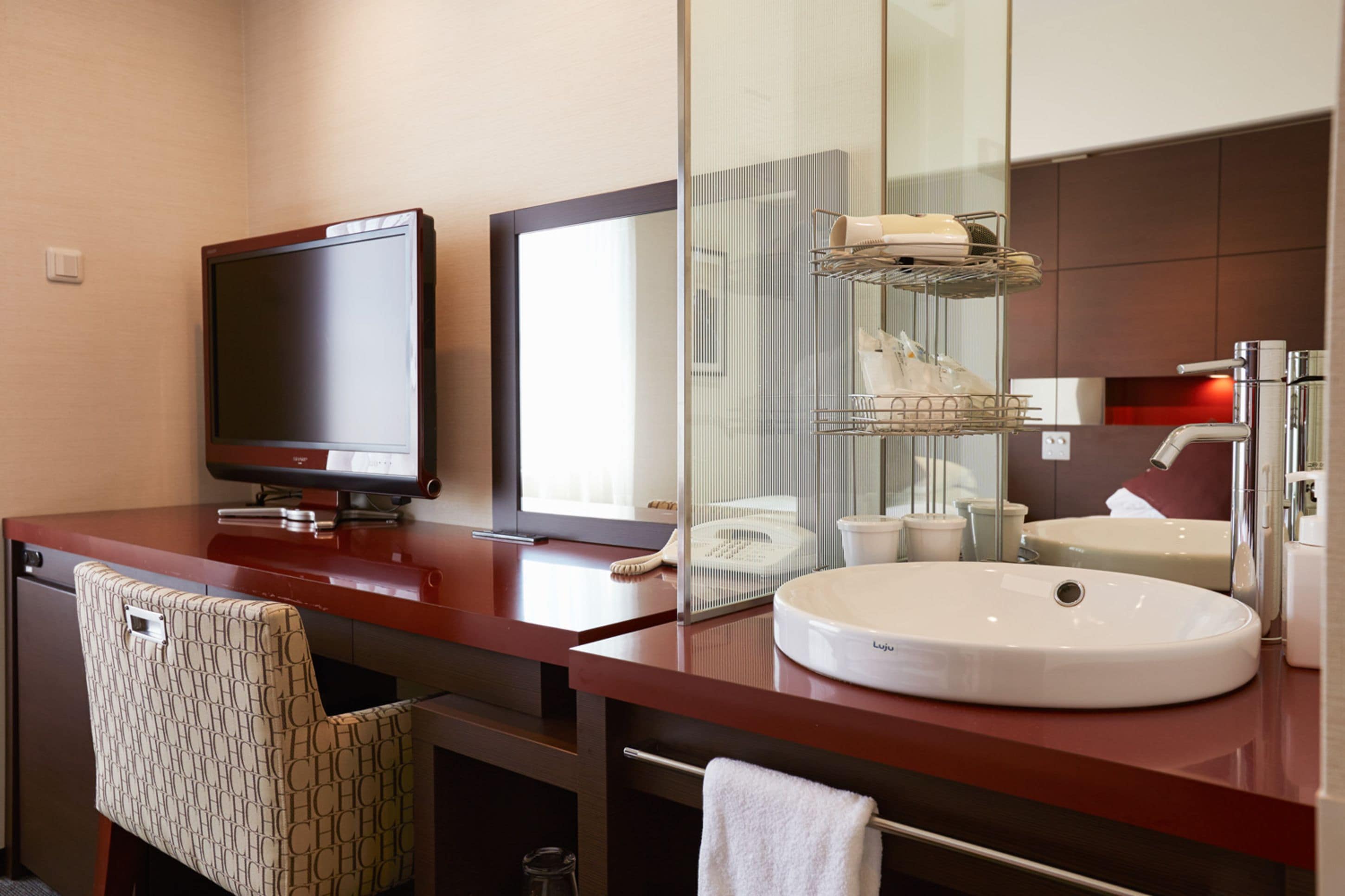 A modern hotel bathroom with a large mirror, a flat-screen TV, a sink, and a towel rack.
