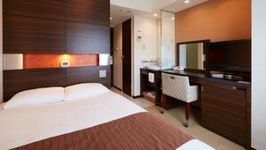 A hotel room with a bed, a desk with a television, a mirror, and a bathroom.