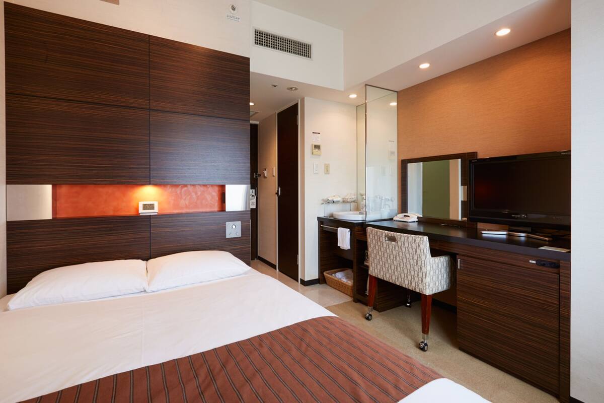 Una habitación de hotel con cama, escritorio con televisor, espejo y baño.