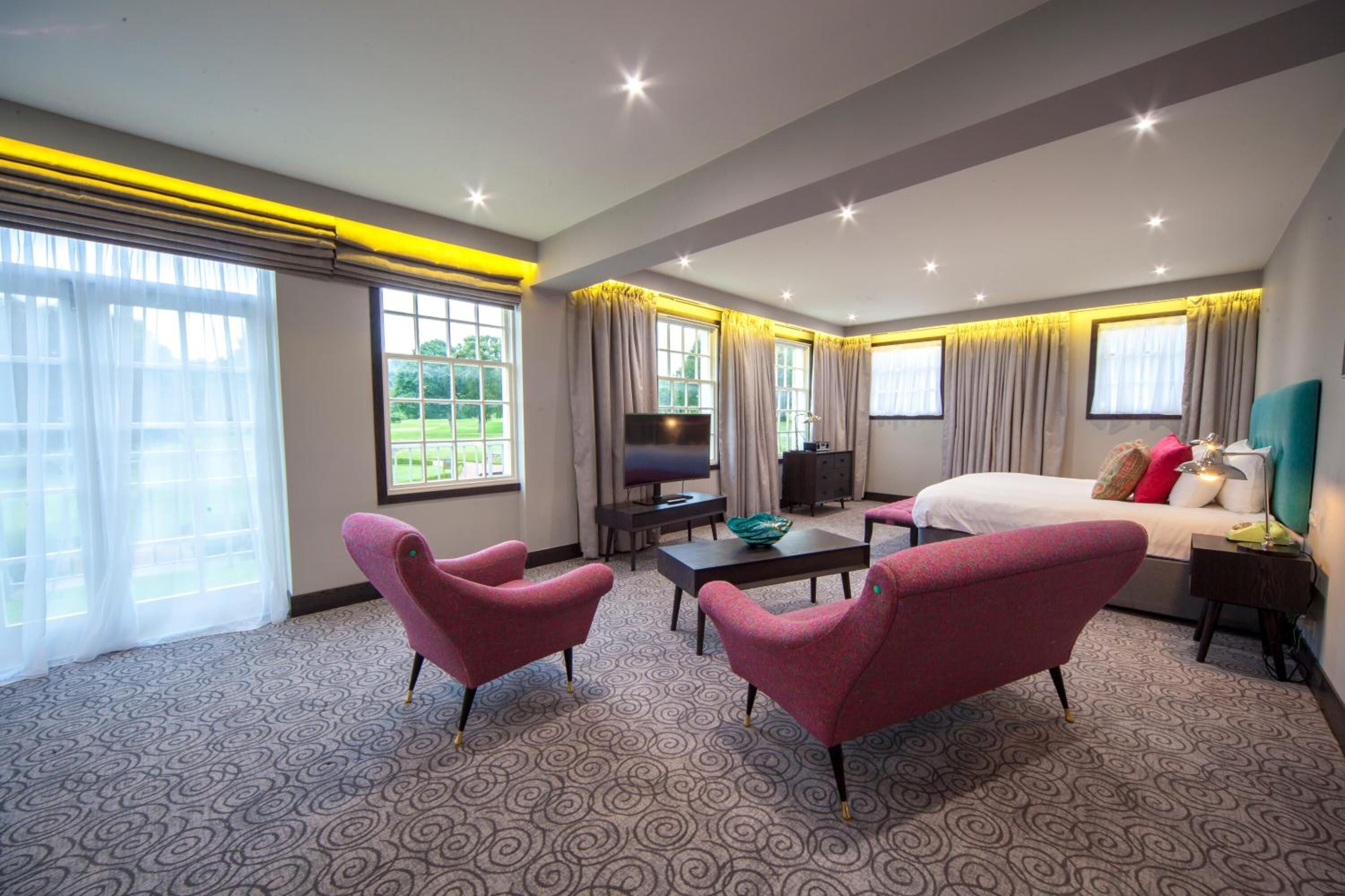 Een moderne hotelkamer met een groot bed, een televisie, een bureau en twee fauteuils.