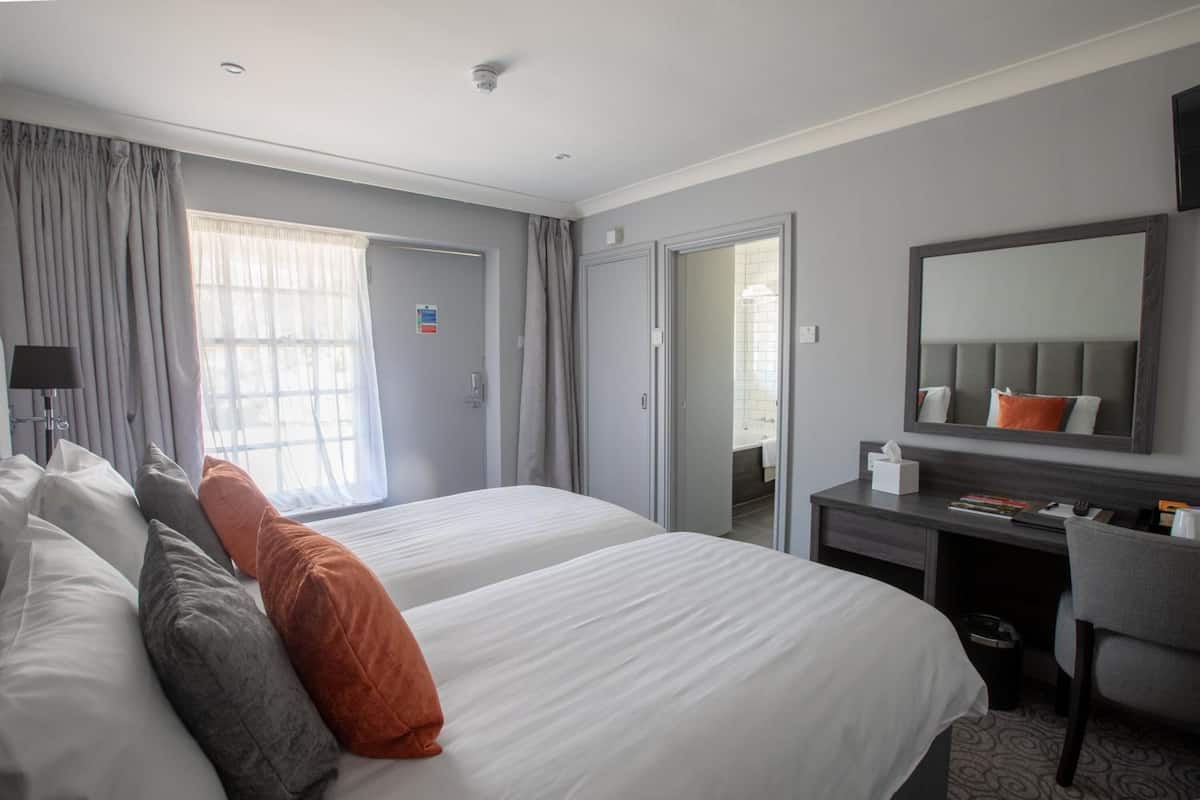 A hotel room with two beds, a desk, a chair, a mirror, and a bathroom door.
