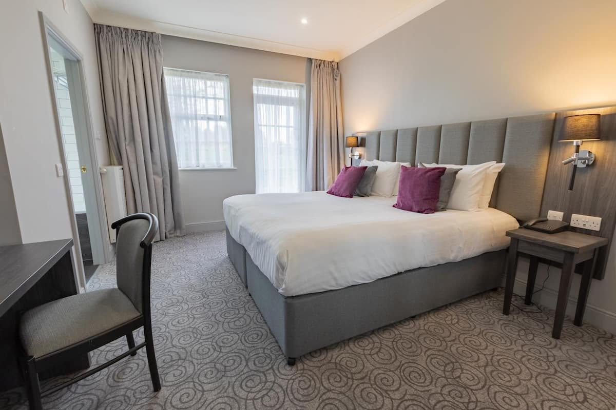 A hotel room with a large bed, a desk, and a chair.