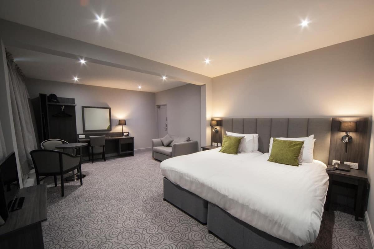 A hotel room with a large bed, a desk, a chair, a TV, and a wardrobe.