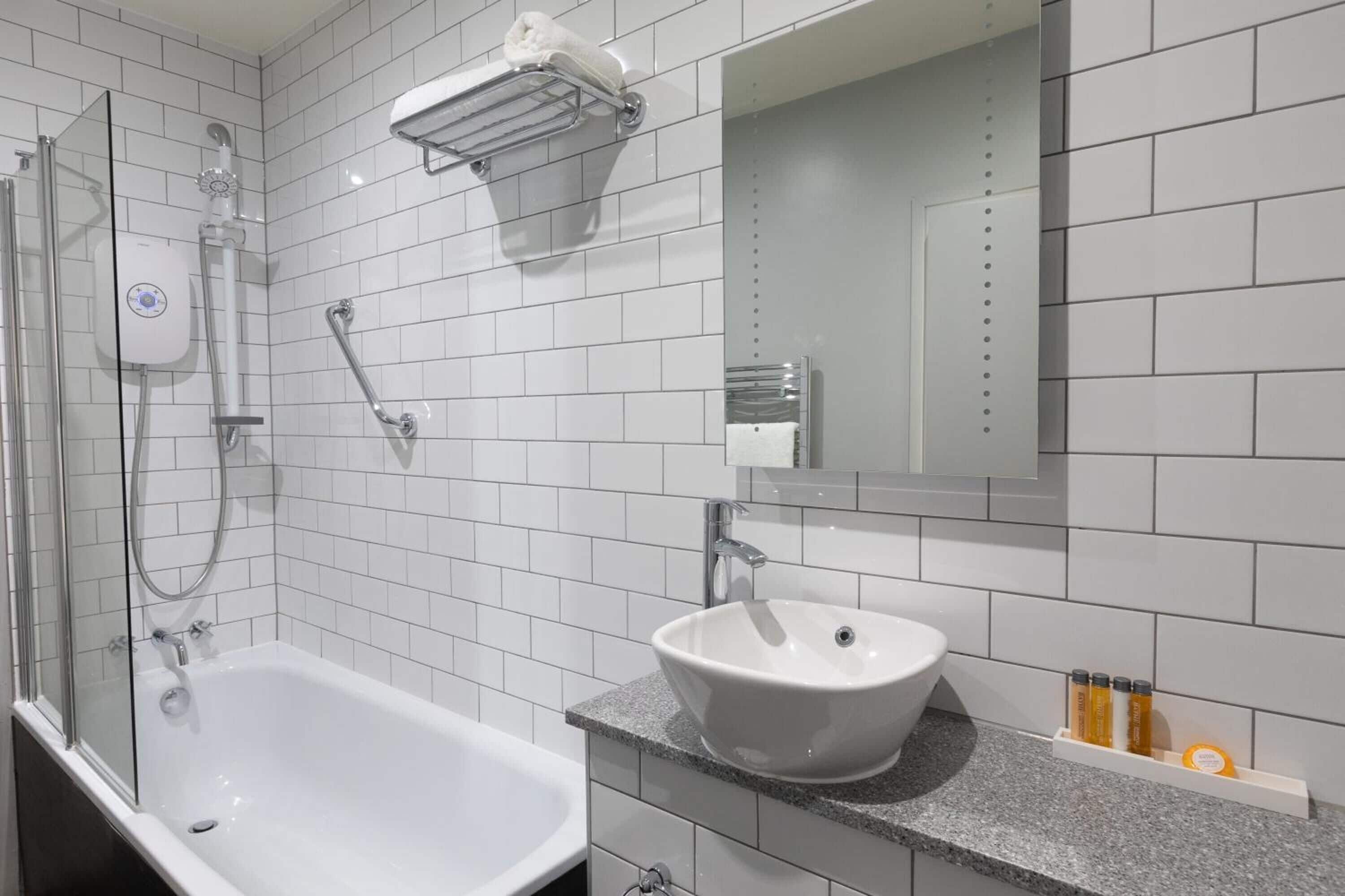 Un baño moderno con una bañera blanca, un lavabo con encimera de granito y una ducha con mampara de vidrio.