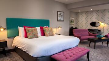 Una habitación de hotel moderna con una cama grande, un sillón rosa, una mesita y una alfombra estampada.