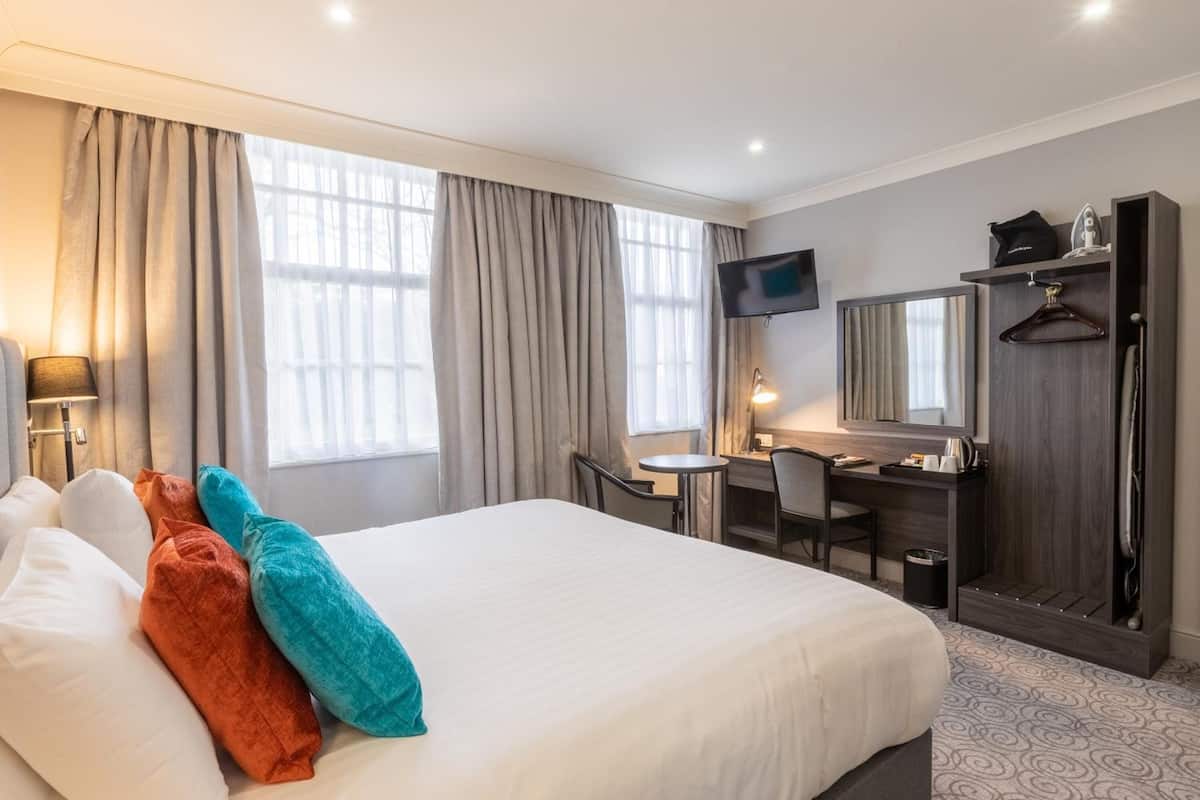 A hotel room with a large bed, a desk, a chair, a TV, a wardrobe, and a mirror.