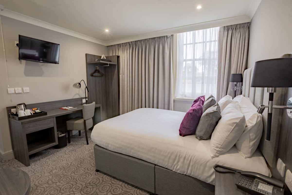 A hotel room with a bed, desk, chair, TV, and a window with curtains.