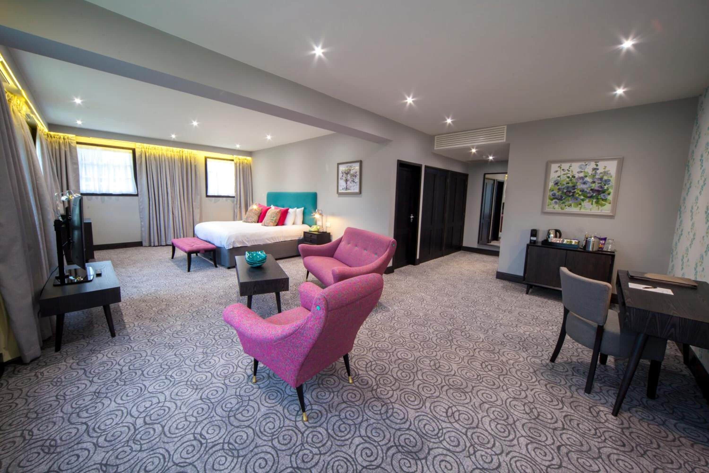 A hotel room with a bed, a desk, a chair, a small table, and a TV.