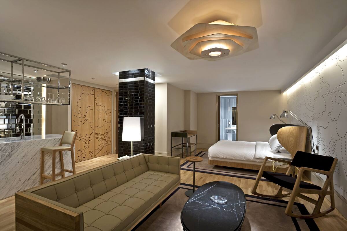 Una habitación de hotel moderna con sofá, mesa de comedor, cama y una cocina visible a través de una puerta abierta.
