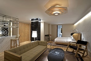 Una habitación de hotel moderna con sofá, mesa de comedor, cama y una cocina visible a través de una puerta abierta.