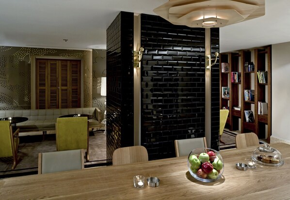 A dining area with a wooden table, chairs, a clear glass bowl with apples, and a bookcase with books. - Witt Istanbul Hotel (Istanbul)