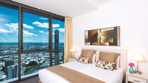 A hotel room with a large bed, a city view, a painting on the wall, and a nightstand with a lamp. - Oaks Brisbane Aurora Suites (Brisbane)