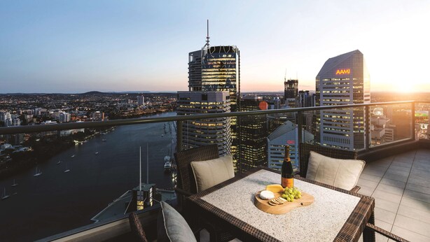 A balcony with a table set for dining, overlooking a cityscape with modern buildings and a river. - Oaks Brisbane Aurora Suites (Brisbane)