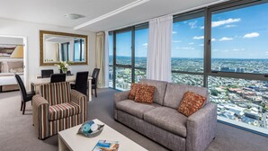 A modern hotel room with a large window offering a city view, a striped sofa, a dining area, and a mirror. - Oaks Brisbane Aurora Suites (Brisbane)