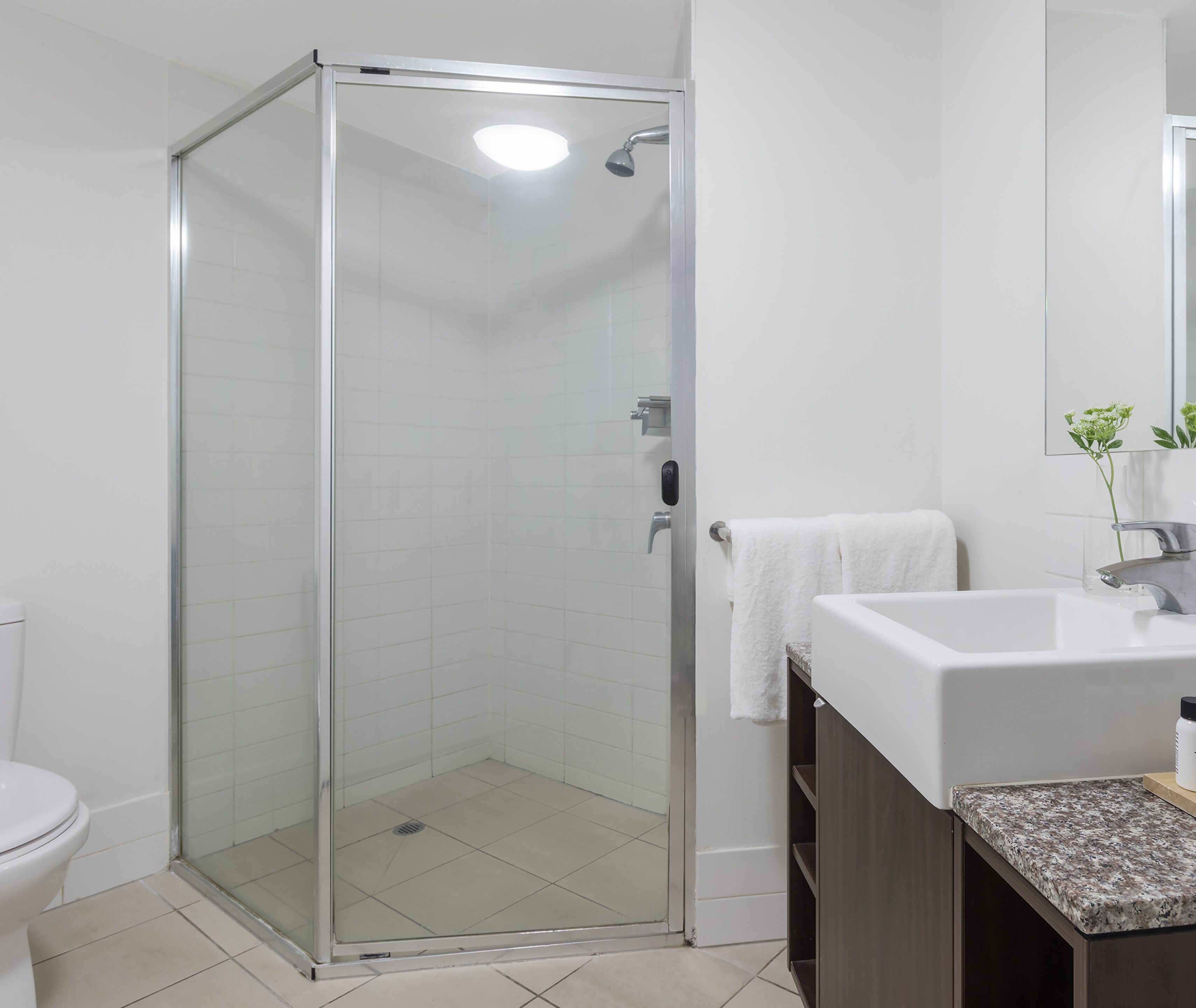 Un baño moderno con ducha acristalada, lavabo blanco y encimera de mármol.