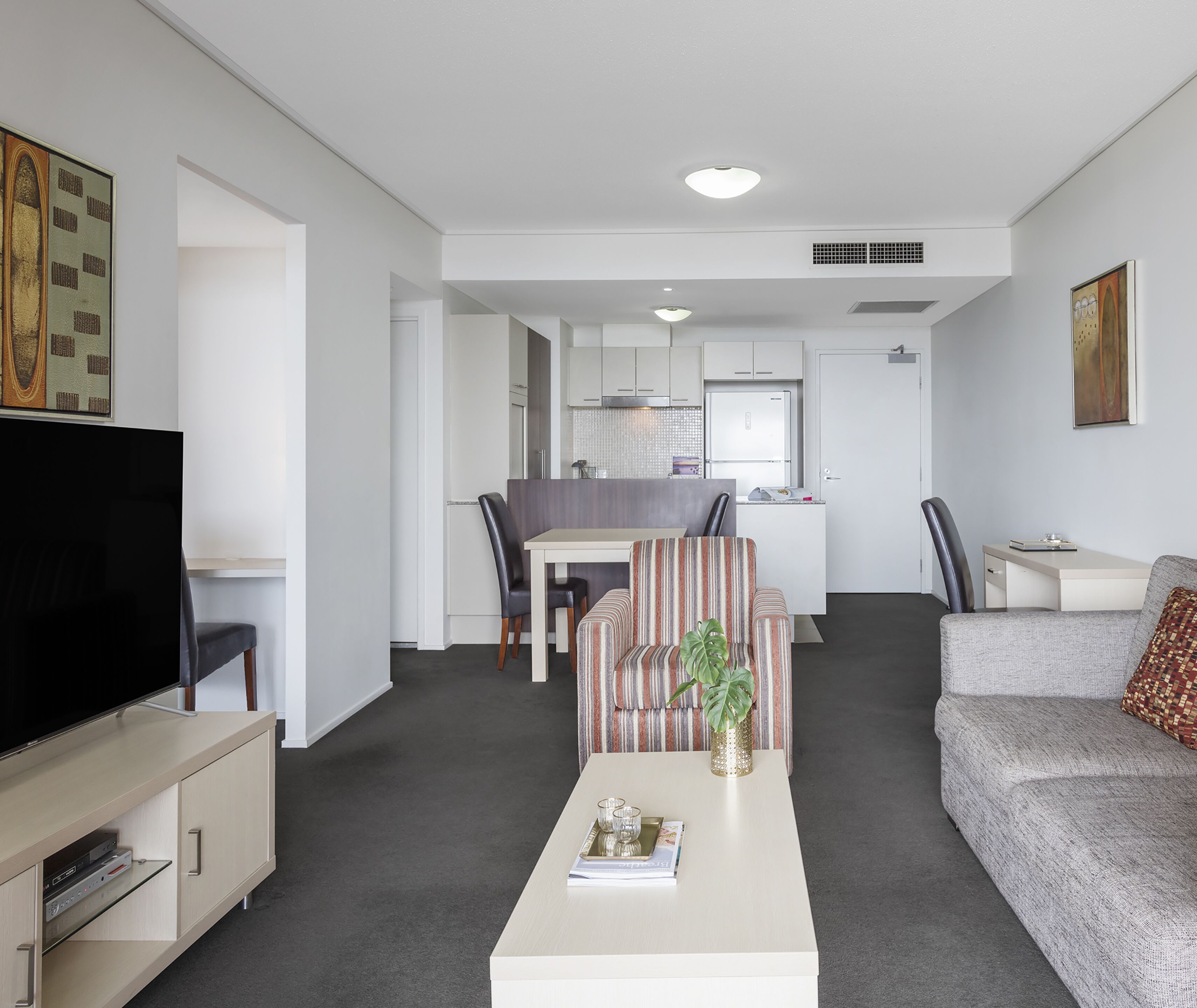 A modern living room with a flat-screen TV, a sofa, a coffee table with decorative items, and a dining area with chairs and a table.