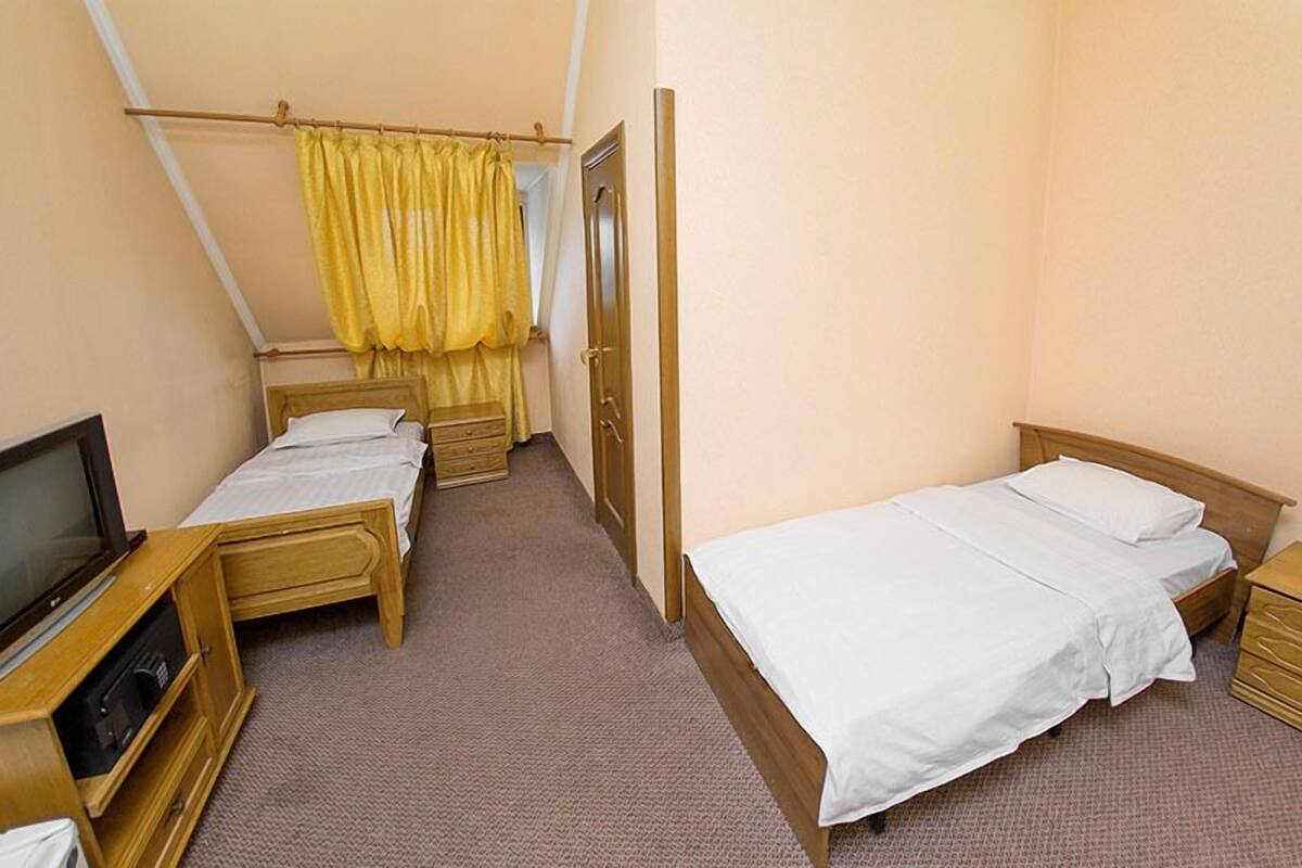 A small, clean room with two single beds, a wooden dresser, a television, and a telephone.
