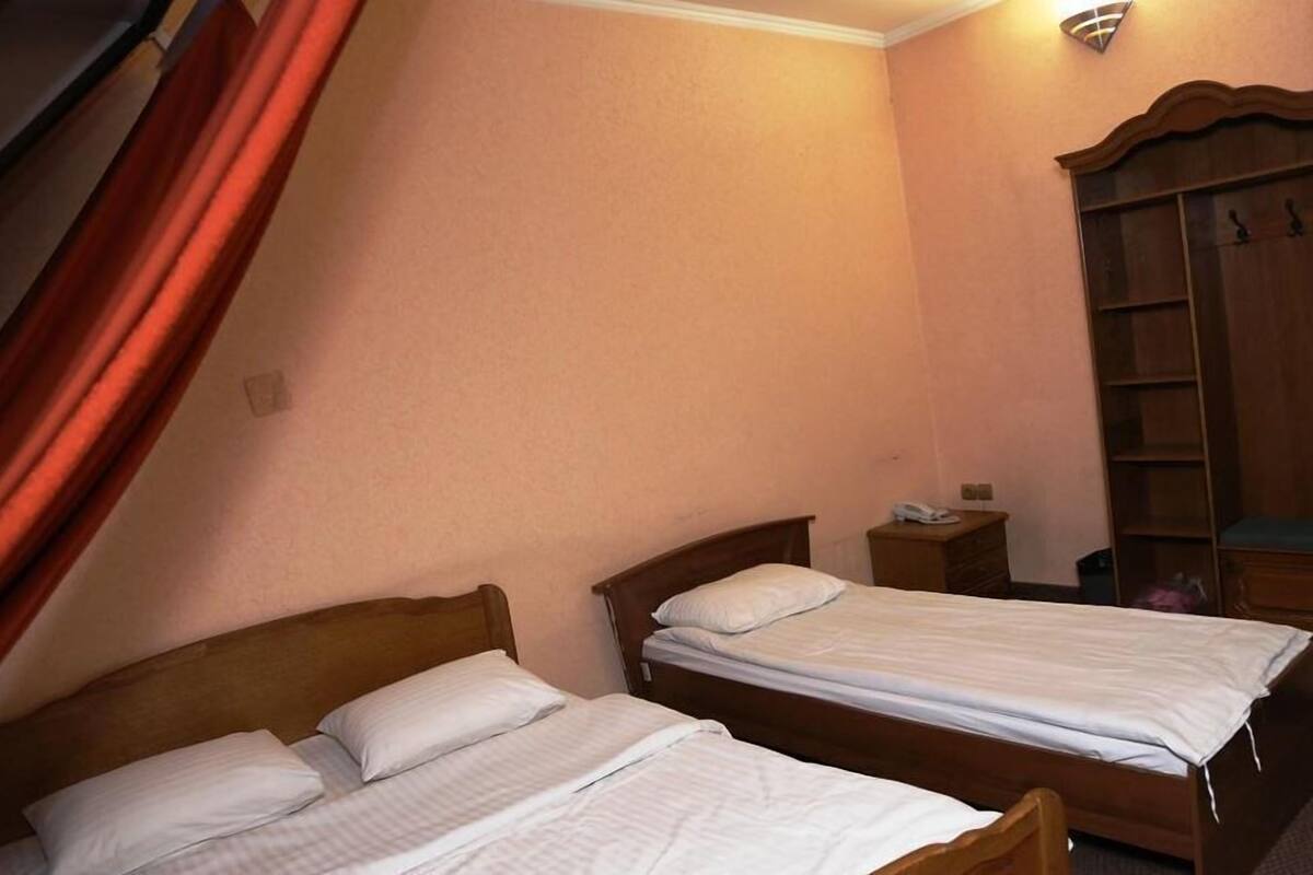 A room with two wooden beds, a nightstand, a wardrobe, and a wall-mounted light fixture.
