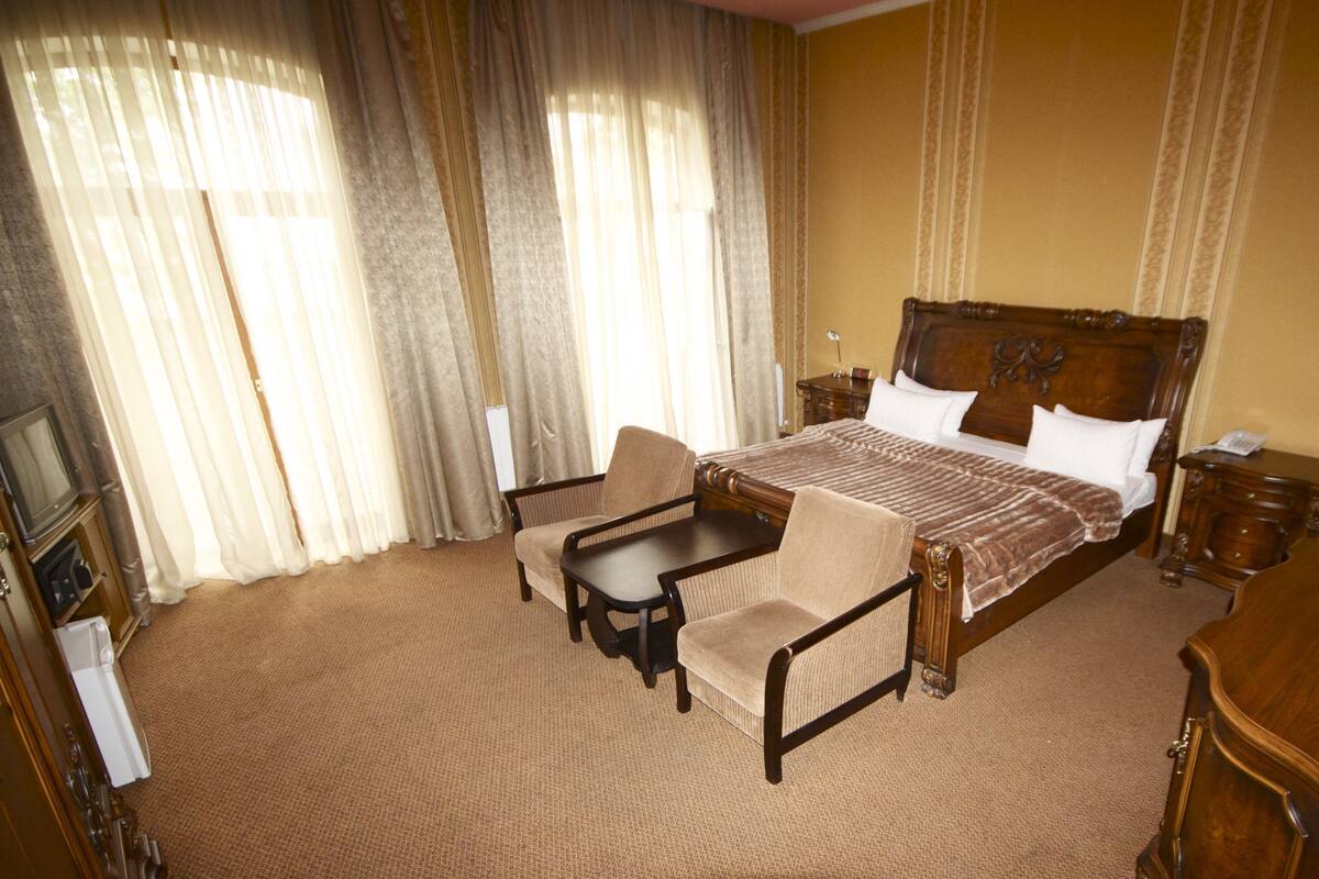 A hotel room with a large bed, two armchairs, a small table, and a wooden nightstand.