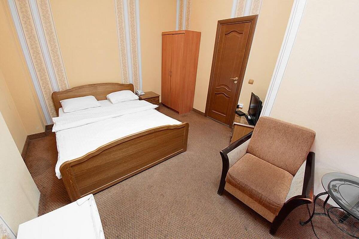 A hotel room with a wooden bed, a chair, a small table, and a wardrobe.