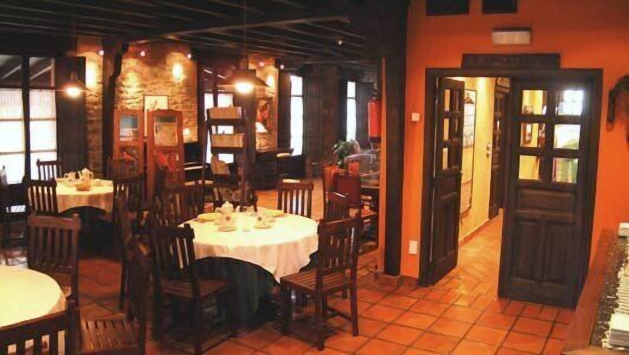 A restaurant with round tables and wooden chairs, stone walls, and a tiled floor.